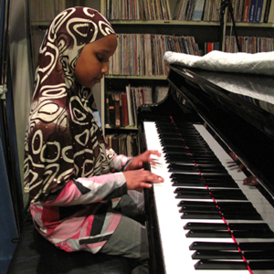 Sideview of a student in hijab playing a piano.
