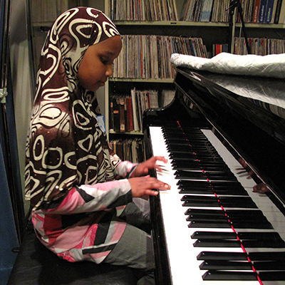 A black girl in a patterned hijab playing the piano.