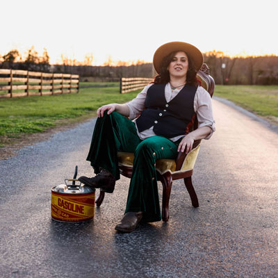Tai Shan on a chair in the middle of a country road, one foot on a can of gasoline.