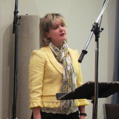 Cherie Hughes standing at a music stand, with a microphone stand in front of her.