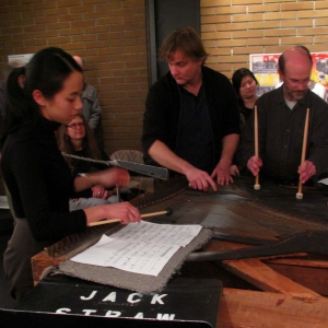 One woman and two men are performing music around an old piano