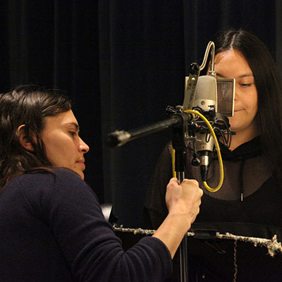A woman adjusts the microphone while a student waits behind the mic