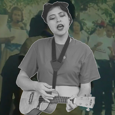 black and white image of karinyo playing an ukulele and singing, superimposed over a blurry image of people standing and singing