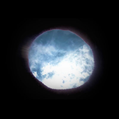 A rough circle showing clouds and blue sky, surrounded by blackness