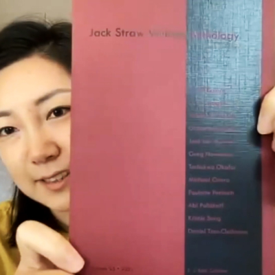 EJ Koh holds up a copy of the 2021 Jack Straw Writers Anthology, in a video still.