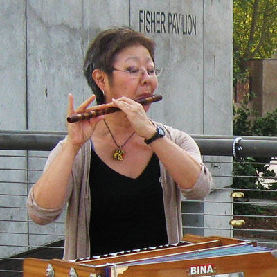Esther Sugai playing a wooden flute, standing outside