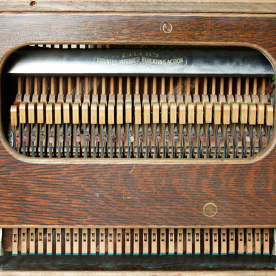 Close-up view of an instrument made from the parts of a piano. Wooden box with man small moving parts inside.