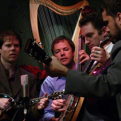 Members of Captain Gravel holding stringed instruments, in front of a harp