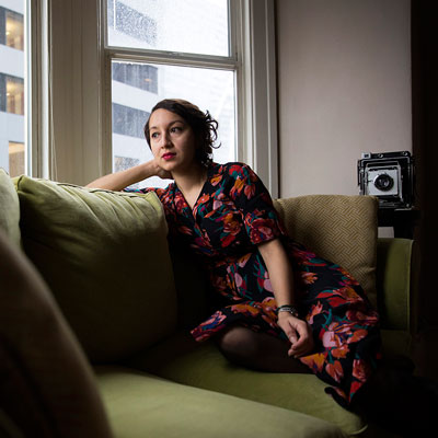 Marilyn Montúfar sitting on a green couch, light coming in from windows on the right.