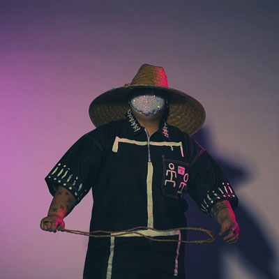 So'le Celestial, wearing a wide straw hat, face mask, and dark clothing, dimly lit in purple