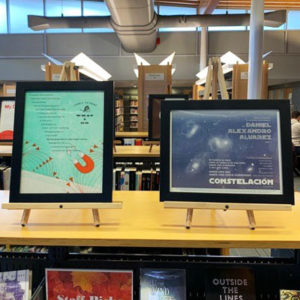 Two broadsides in frames sitting on top of a set of shelves in a library.