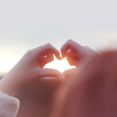 A child's hands making the shape of a heart with the sun shining through it.