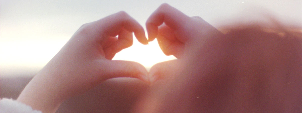 A child's hands making the shape of a heart with the sun shining through it.