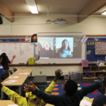 Students watch Sunam Ellis and Brenda Arellano on a projection screen and stretch their arms out.