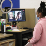 A student stands in front of a computer screen with Sunam Ellis and Brenda Arellano on it.