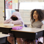 Two students sit at their desks, singing.
