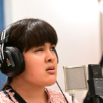 A student wearing headphones sings into a microphone.