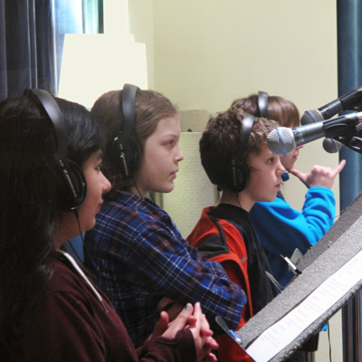 Four students wearing headphones stand at microphones.