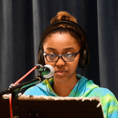 Student wearing headphones and glasses at a microphone.