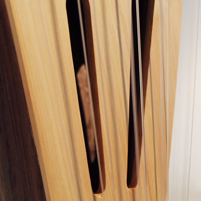 Close-up image of a wooden sculpture with holes and vibrating strings like a musical instrument.