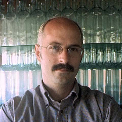 Photo of Jeff Crandall, a wall of glass bottles behind him.