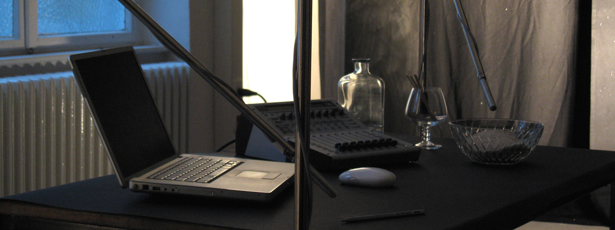 A laptop computer, audio mixing board, and three glass vessels on a tabletop.