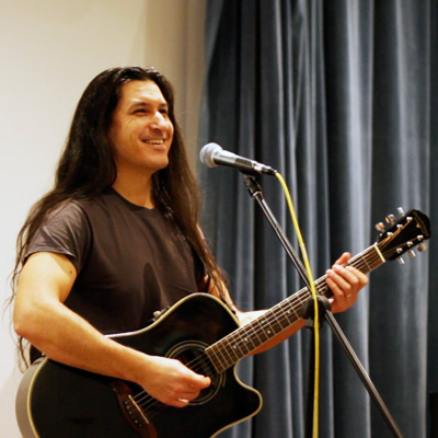 John Osebold standing at a microphone holding an acoustic guitar.