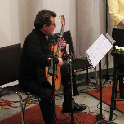 Roberto Limon, seated, playing classical guitar while looking at music on a music stand.