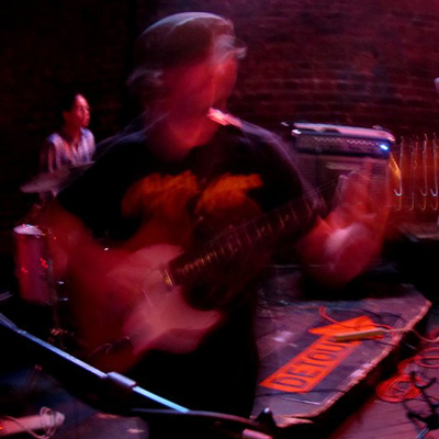 Blurry photo of Skiff Feldspar on stage, holding an electric guitar.
