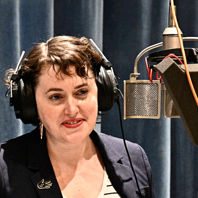 Katharine Strang wearing headphones and standing at a microphone.