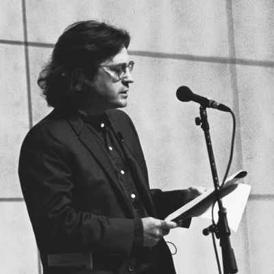 Black and white photo of Kimball MacKay standing at a microphone and reading.