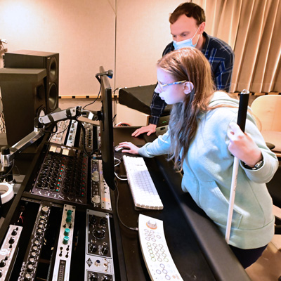 Engineer Daniel Guenther and student holding a white cane standing at a studio computer.