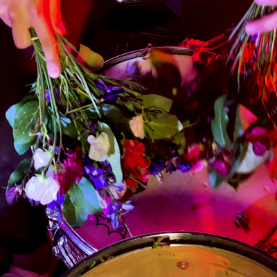 Hands holding plastic flowers, parts of a drum kit.