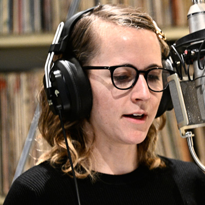 Erin Langer, wearing headphones, speaking into a microphone.