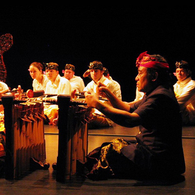 I Wayan Sinti, seated, plays gamelan while others look on in the background.