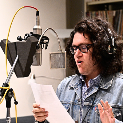 Vincent Rendoni, holding a page and standing at a microphone, wearing headphones.