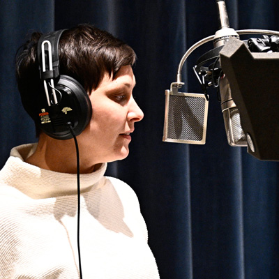 Carrie Beyer, wearing headphones, standing in front of a microphone.