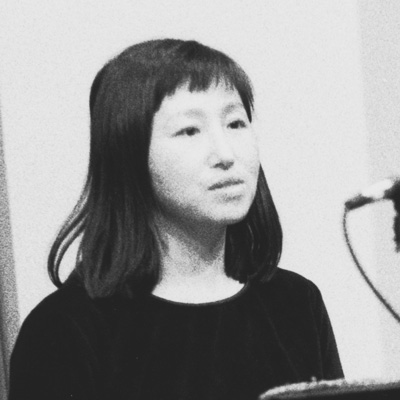 Black and white photo of Don Mee Choi, looking to the right, with a microphone cable in front of her,