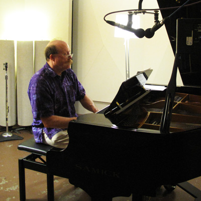 Roger Nelson playing piano, a pair of microphones overhead.