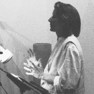 Black and white photo of Rebecca Brown, in profile, speaking with a music stand in front of her.