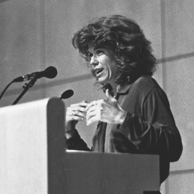 Black and white photo of Trish Ready, standing at a lectern with a microphone.
