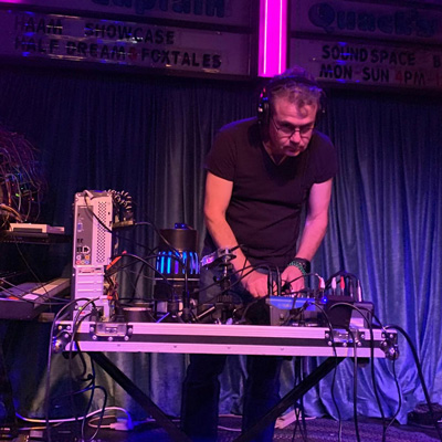 Phot of Alex Keller, standing at a table with several electronic devices connected by cables.