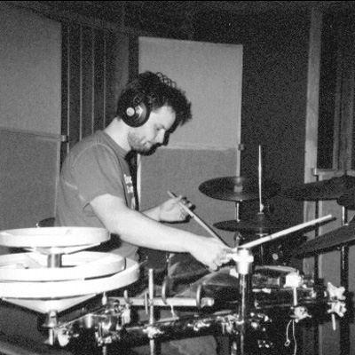 Black and white photo of Bob Rees wearing headphones and playing percussion instruments.