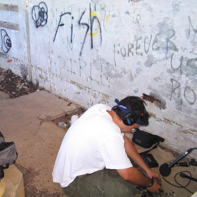 Jon Tulchin sits on the ground with recording equipment, next to a graffiti-covered wall.