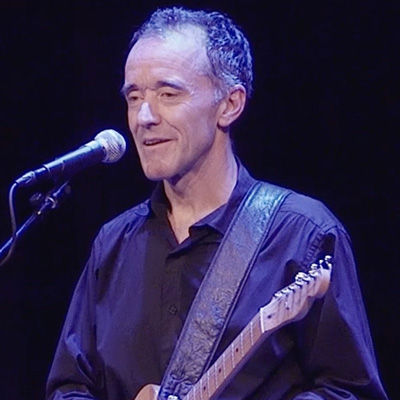 Kevin Joyce standing at a microphone, holding an electric guitar.