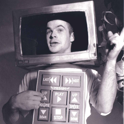 Black and white photo of Mike Leavitt, wearing a cardboard TV head with a panel resembling a remote control on his chest.