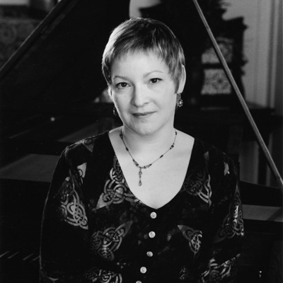 Black and white photo of Tamara Friedman, with a grand piano in the background