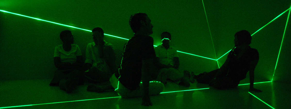 A group of people sitting in a green-light space with laser beams shining across their bodies.