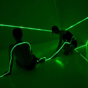 Two performers in a green-light space with laser beams shining across their bodies.