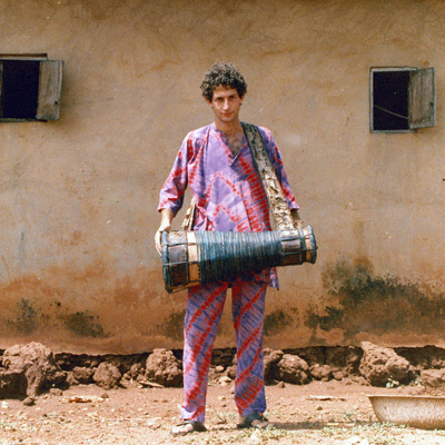 Andy Frankel, wearing colorful clothing and holding a hand drum.